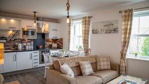 A modern kitchen with a dining area, a sofa, and a window with curtains. - Sandy Bottom Apartment is a 1st floor open plan Appt on The Bay, Filey (Filey)
