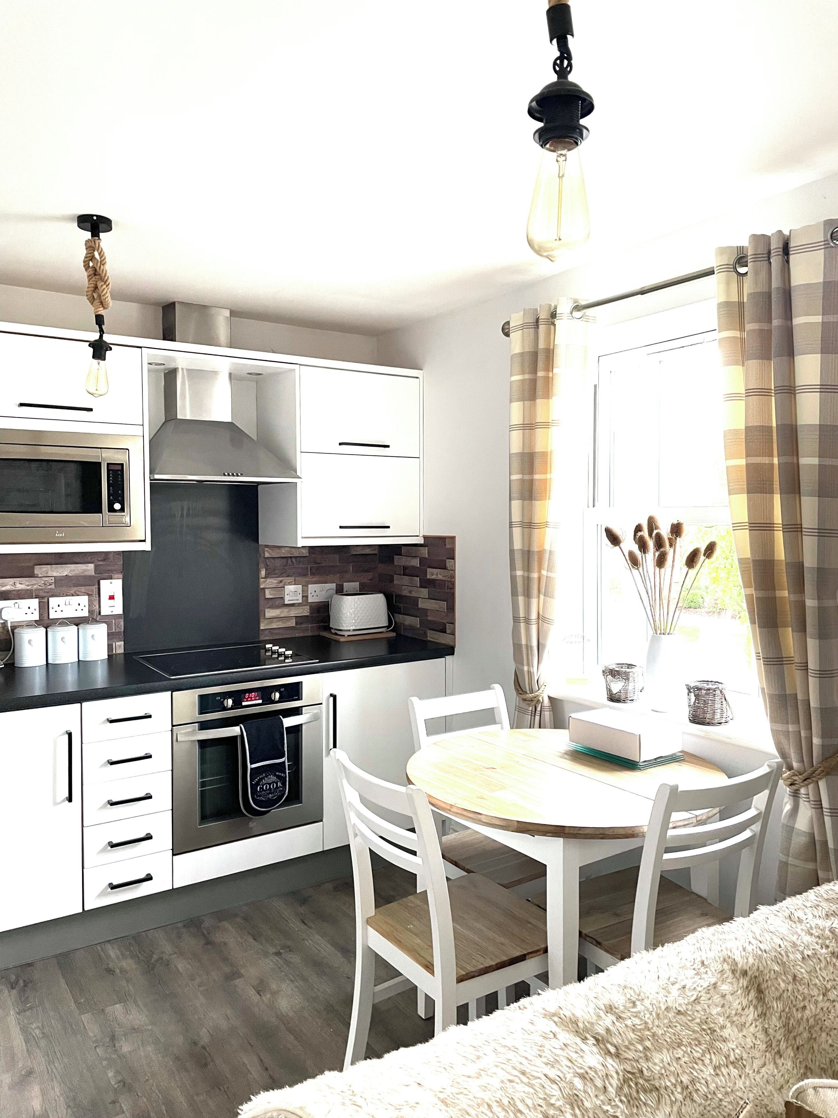 A modern kitchen with white cabinetry, a built-in oven, a microwave, and a gas stove. There is a dining area with a round table and white chairs.
