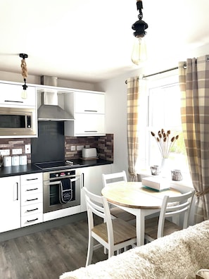 A modern kitchen with white cabinetry, a built-in oven, a microwave, and a gas stove. There is a dining area with a round table and white chairs.