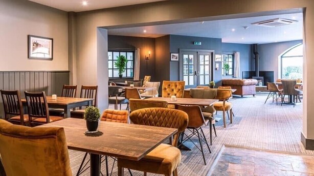 A spacious hotel lobby with multiple seating areas, including a dining area with wooden tables and chairs, a lounge with sofas and armchairs, and a reception desk. - Sandy Bottom Apartment is a 1st floor open plan Appt on The Bay, Filey (Filey)