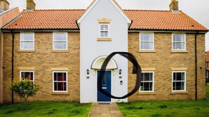 A two-story house with a blue door, multiple windows, and a red-tiled roof. - Sandy Bottom Apartment is a 1st floor open plan Appt on The Bay, Filey (Filey)