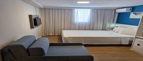 A hotel room with a bed, a sofa, a TV, and a window with curtains.