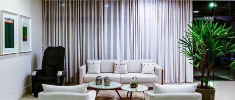 A modern living room with a white sofa, two white armchairs, a black chair, a coffee table, and a potted plant.