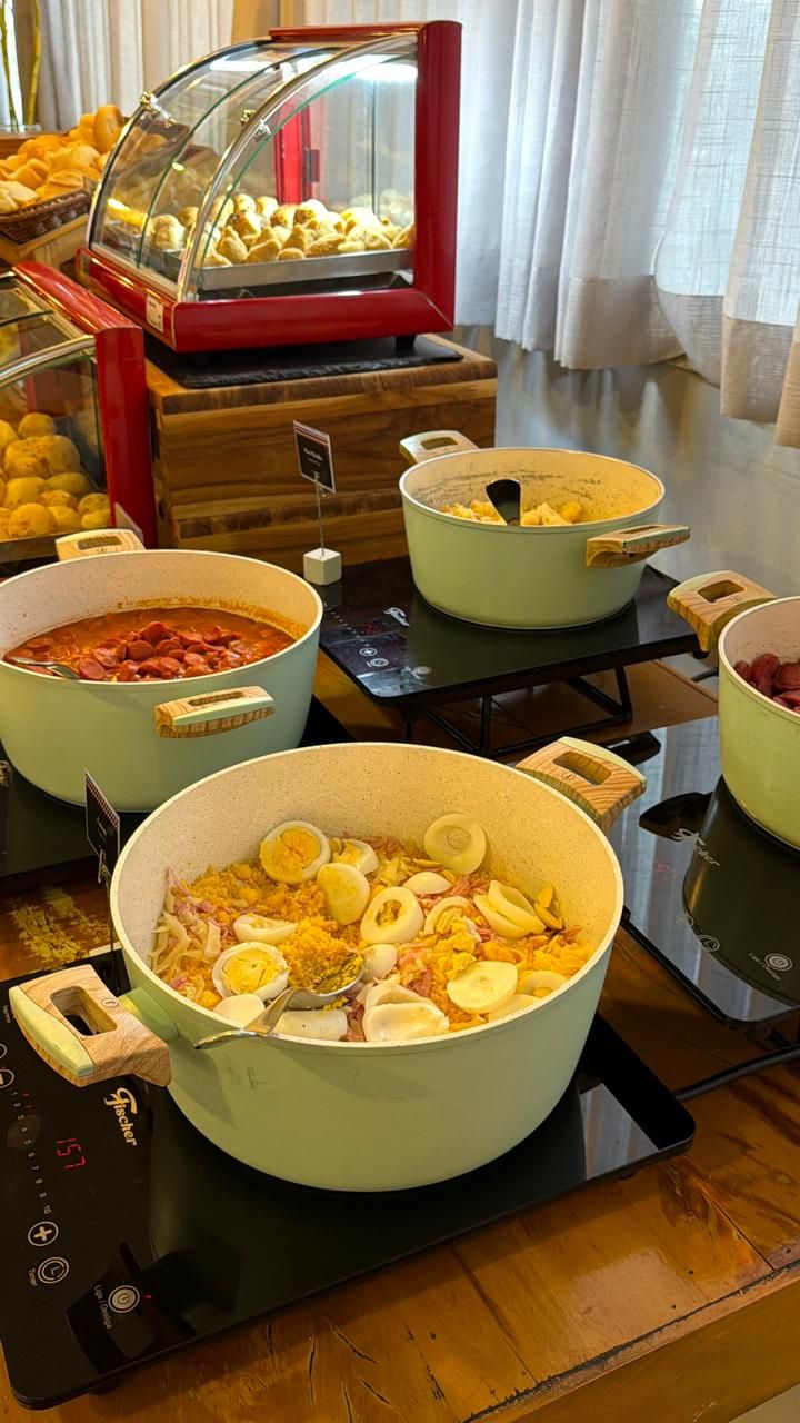 A buffet setup with various dishes, including a large pot of rice with eggs, a pot of chili, and a display case with pastries.