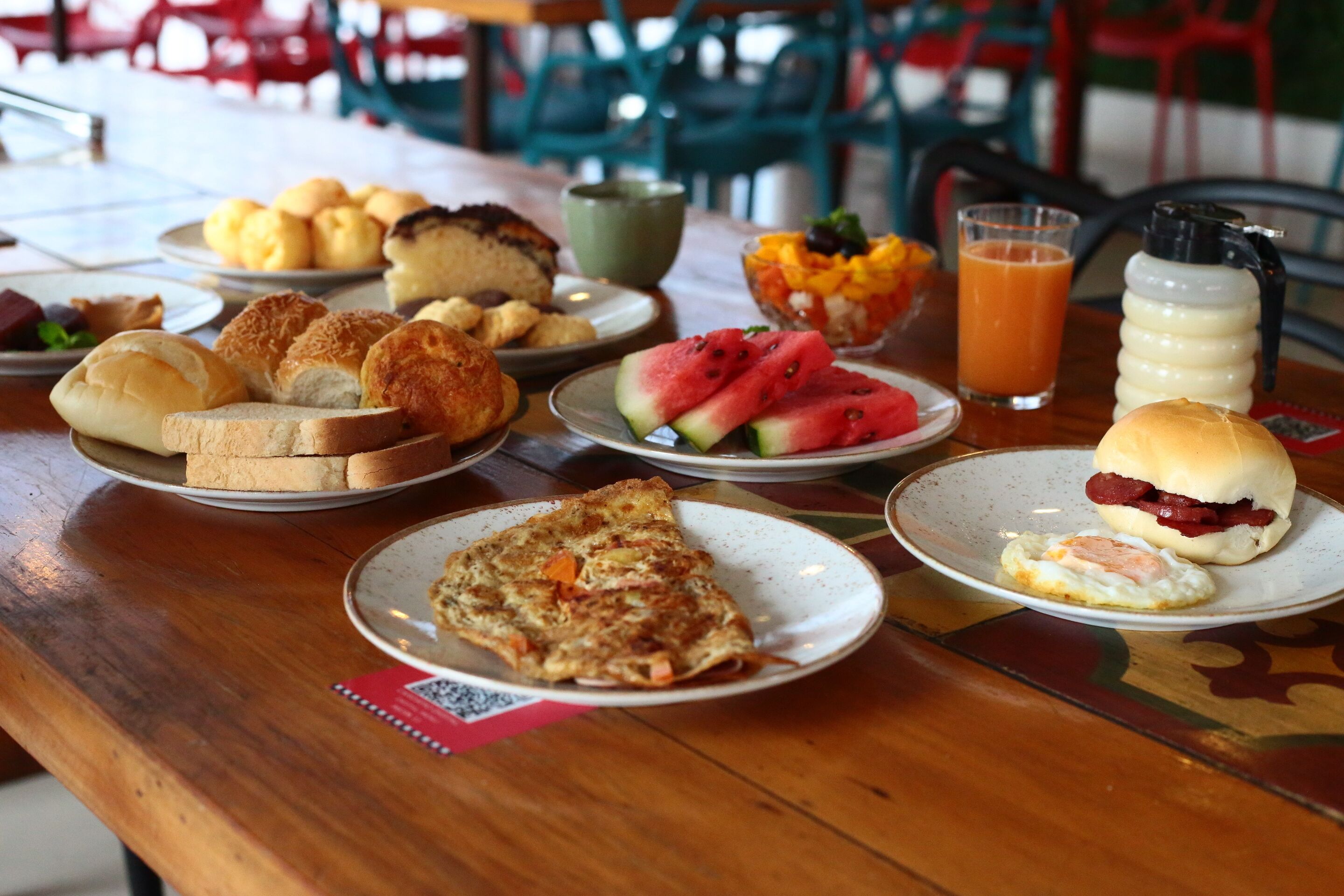 Une table de petit-déjeuner avec divers aliments, un verre de jus d’orange et un thermos.