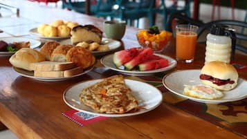 A breakfast table with various food items, a glass of orange juice, and a thermos.