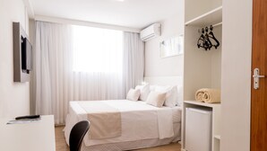 Habitación de hotel con cama, escritorio, silla, televisor, aire acondicionado, armario y un refrigerador pequeño.