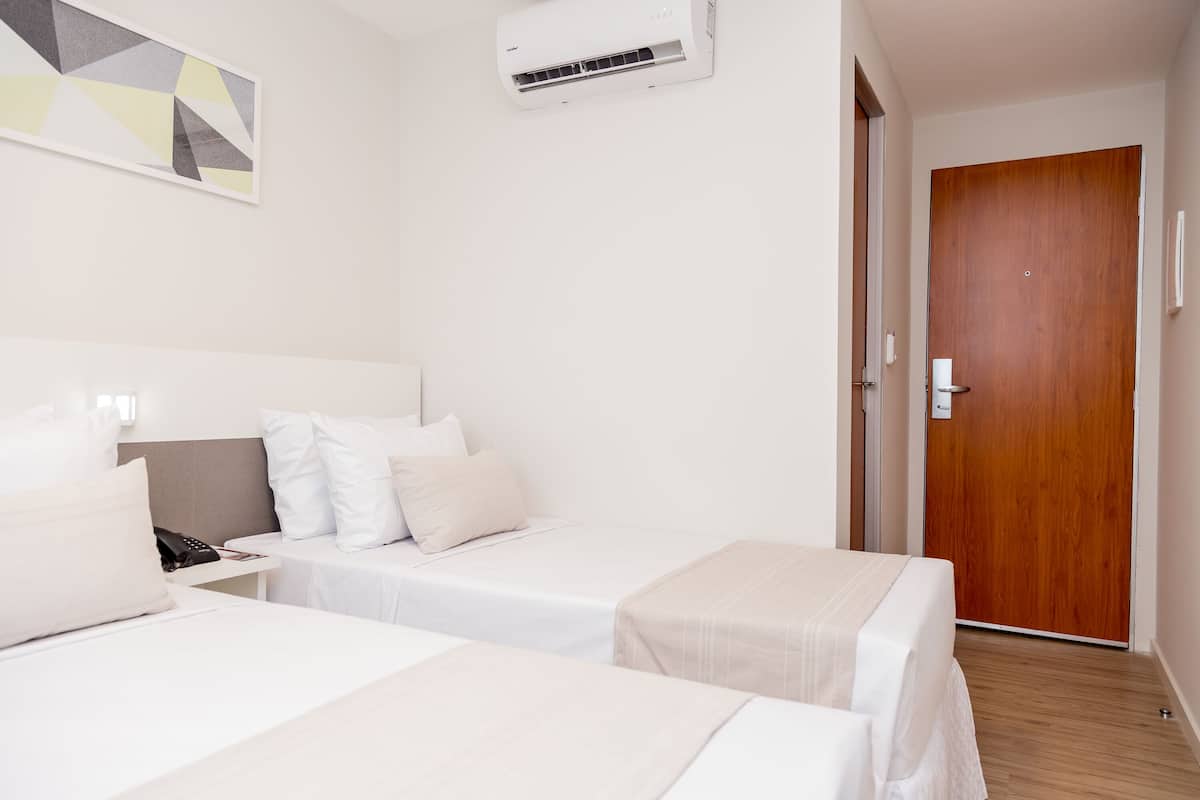 A hotel room with two single beds, a wooden door, and a wall-mounted air conditioner.