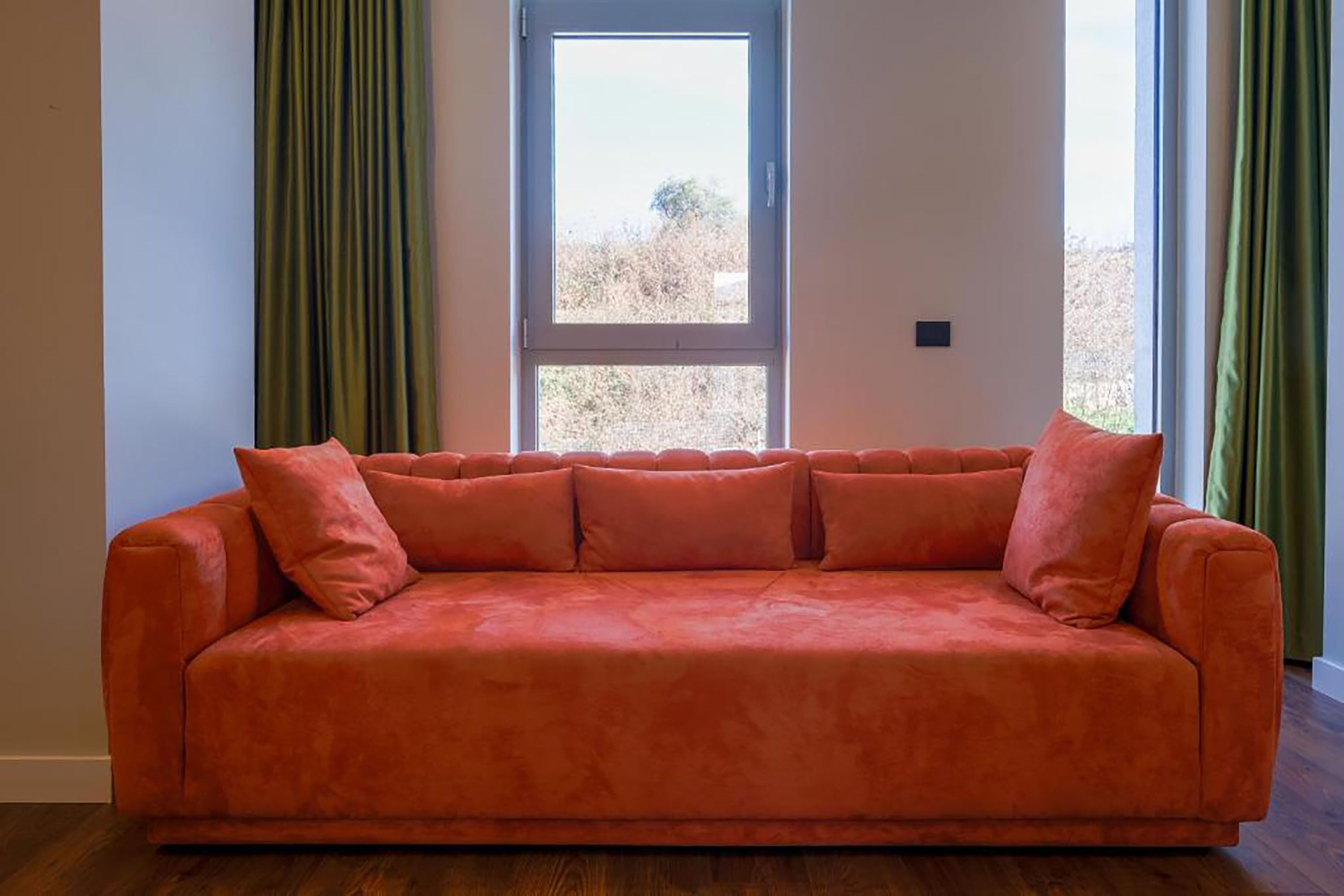 Una habitación con un sofá rojo, una ventana y cortinas verdes.