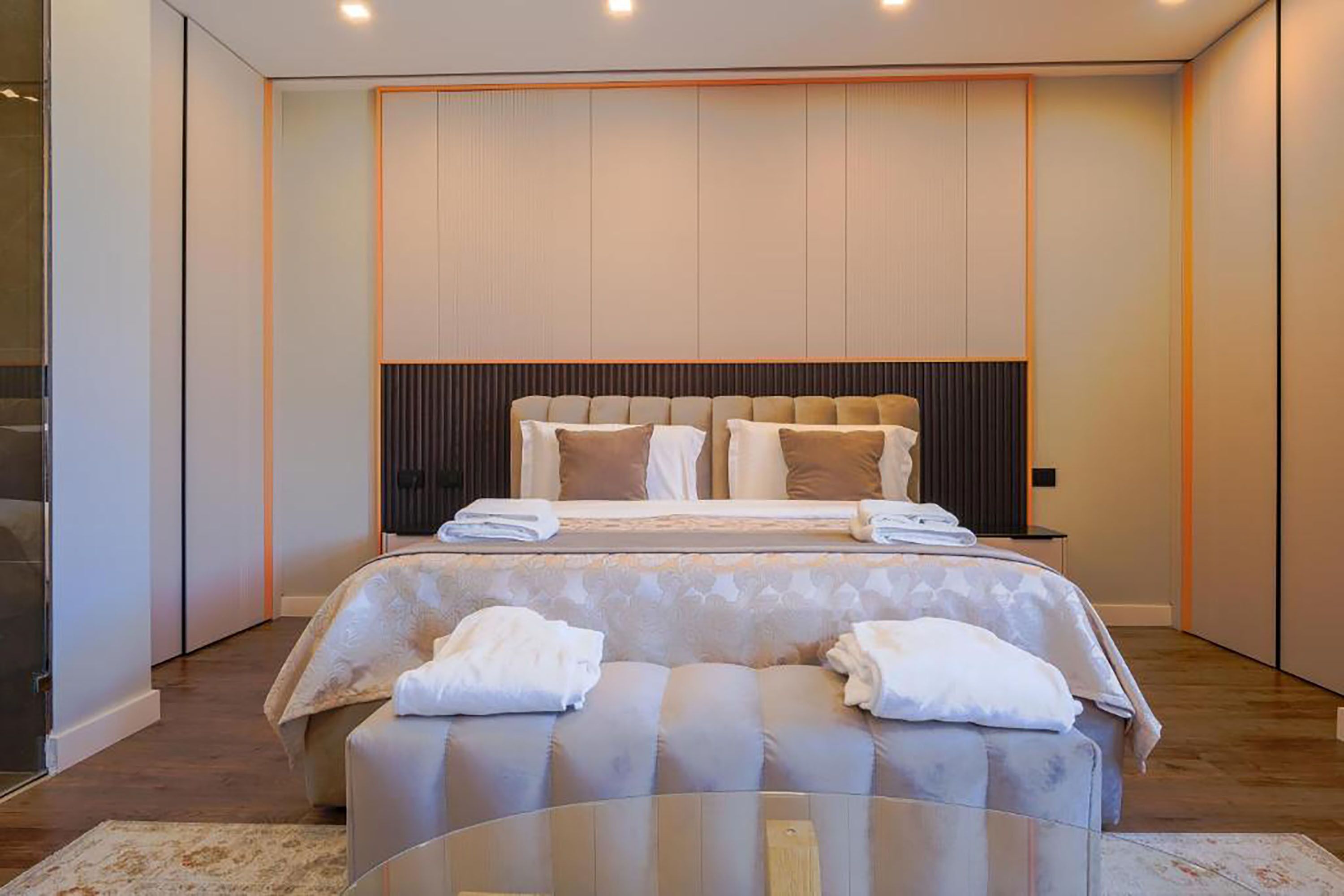 Un dormitorio moderno con una cama grande, una mesita de noche y un área de descanso con una mesa de vidrio.