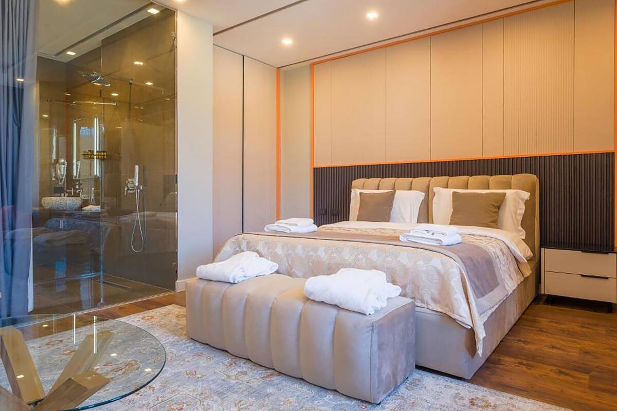 A modern bedroom with a large bed, a glass shower enclosure, and a round glass table.