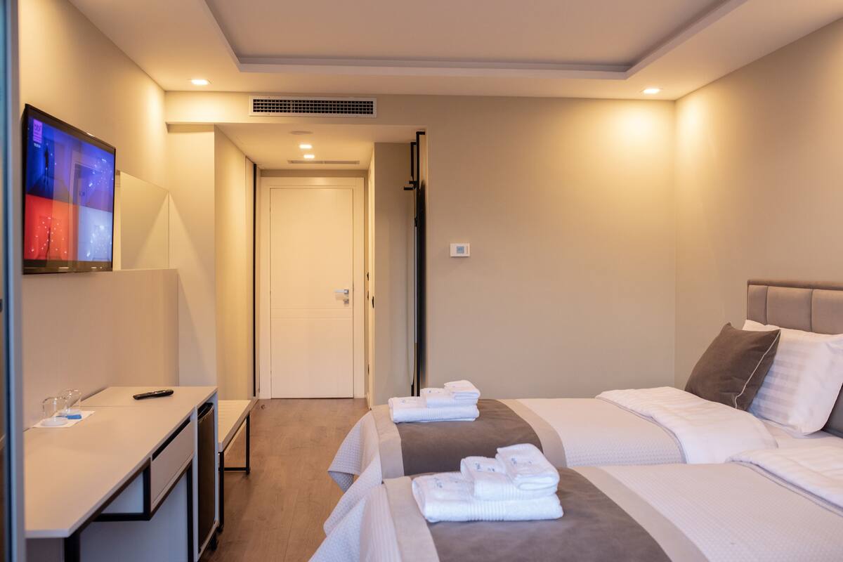 A hotel room with a desk, two beds, and a TV on the wall.