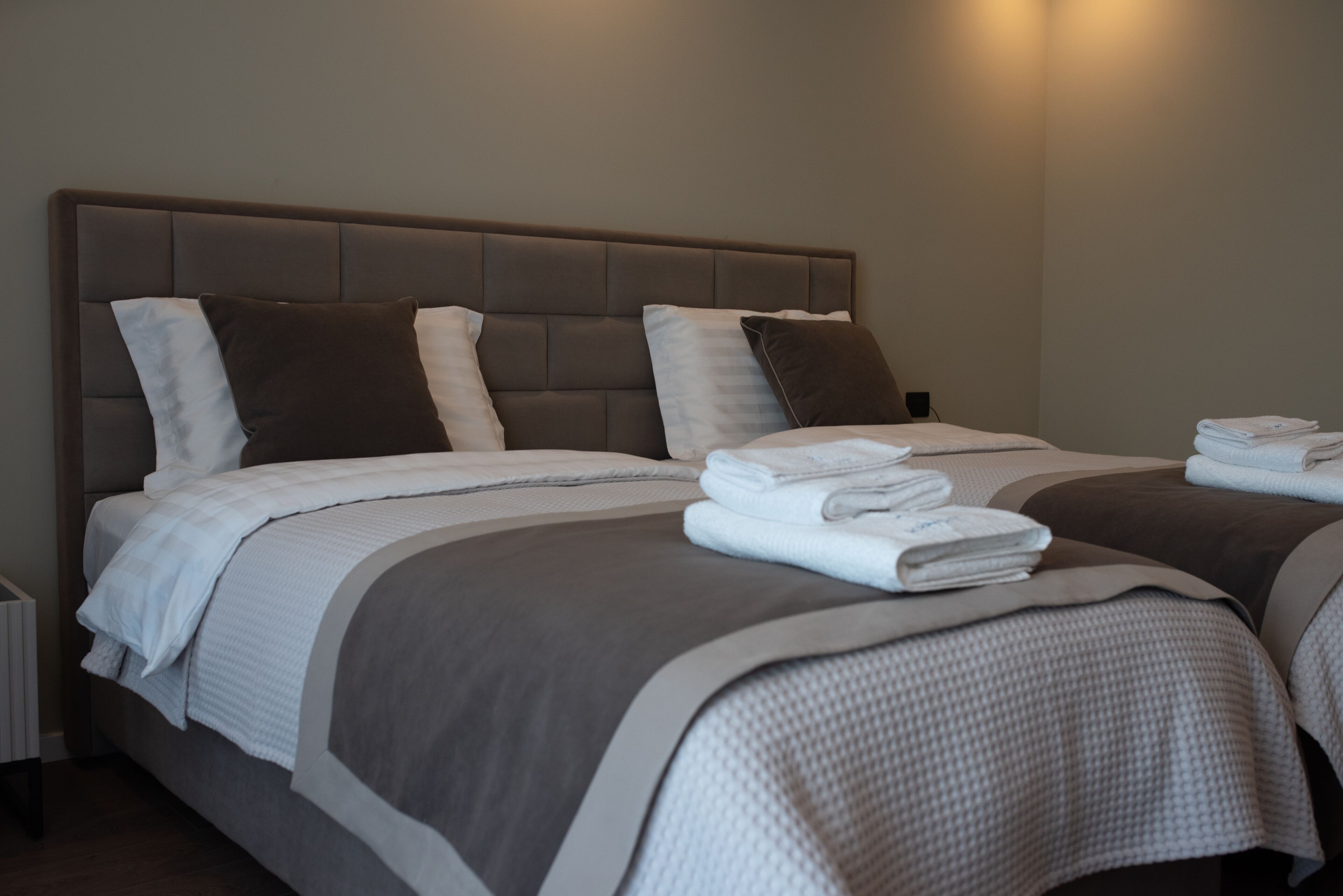 Habitación de hotel con dos camas, cada una con cabecera, ropa de cama blanca y toallas dobladas sobre las camas.