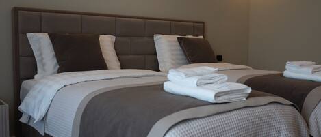 Habitación de hotel con dos camas, cada una con cabecera, ropa de cama blanca y toallas dobladas sobre las camas.