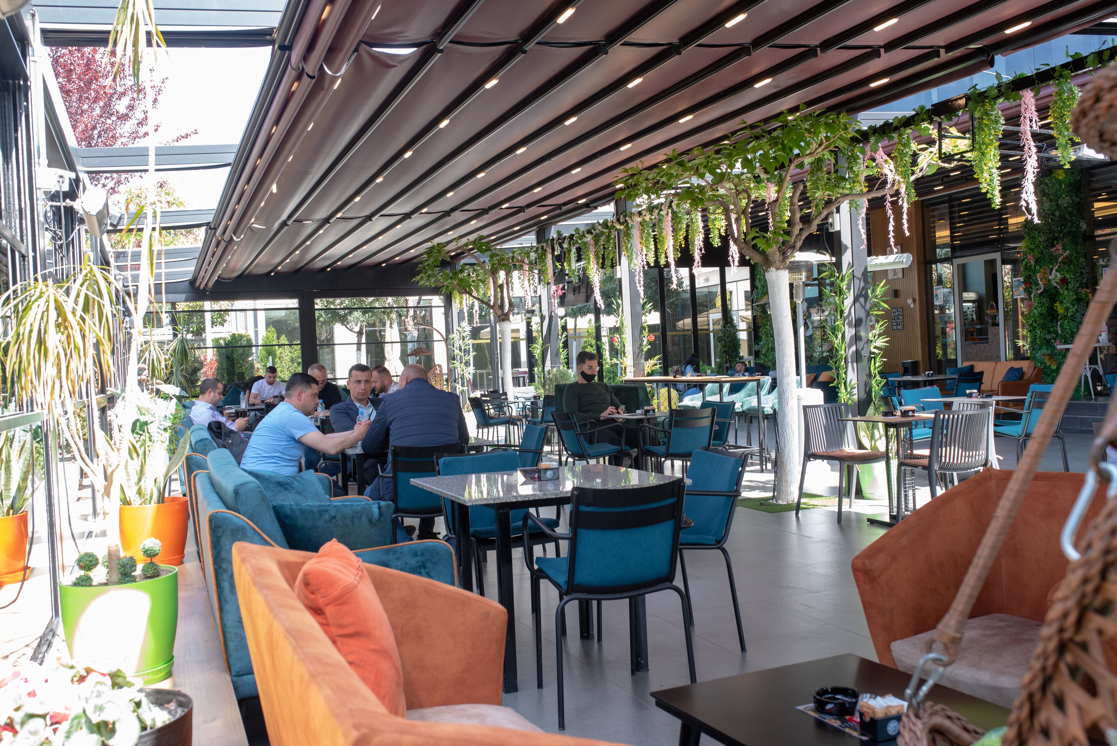 An outdoor cafe with seating arrangements, tables, and potted plants.