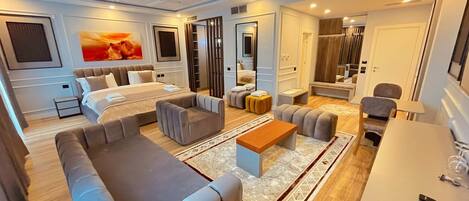 A modern hotel room with a large bed, a sofa, a coffee table, and a desk.