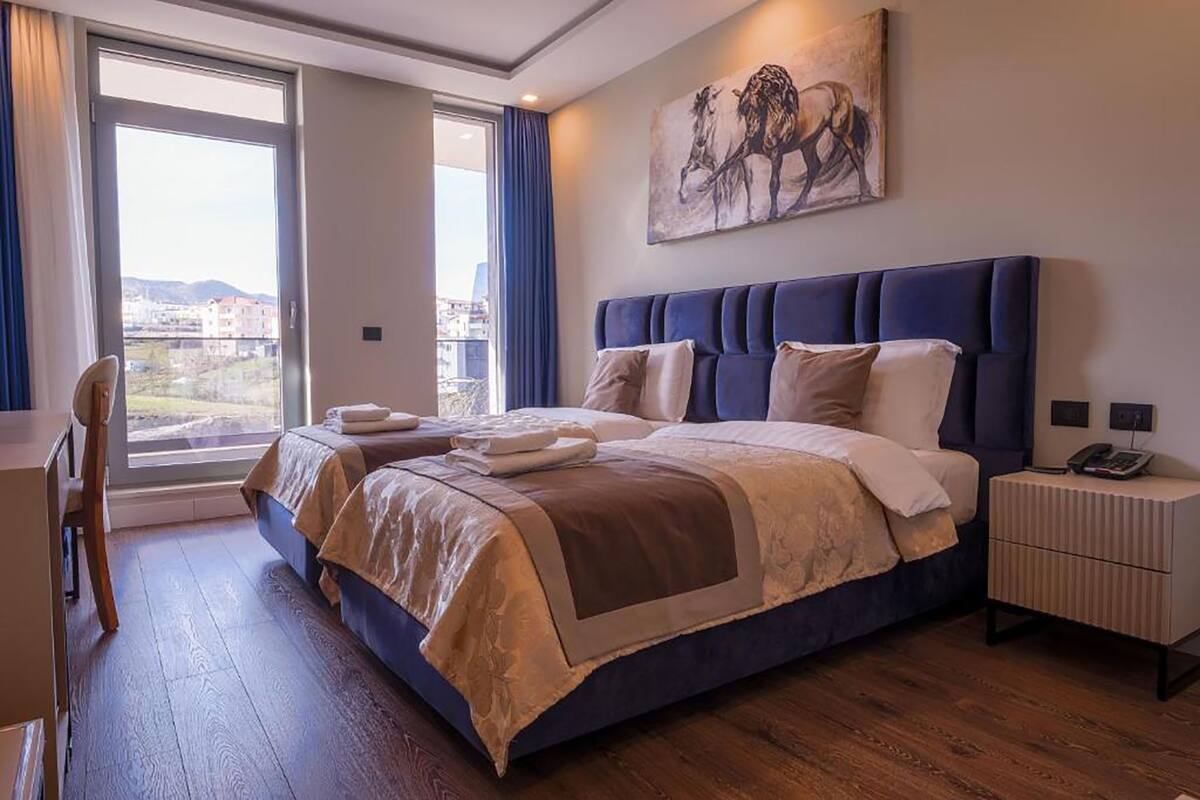 A modern hotel room with a large bed, a desk, and a view of the city.