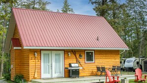 Eine Blockhütte mit rotem Dach, einer Veranda mit Sitzgelegenheit und einem Grill.