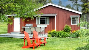 Una cabaña roja de madera con un porche, una parrilla y dos sillas Adirondack.