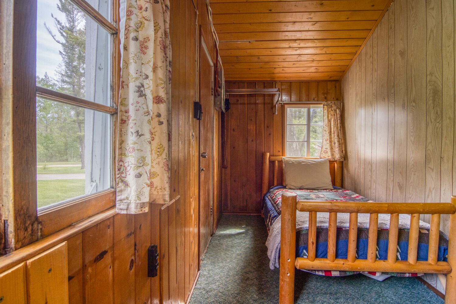 A wooden cabin room with a bed, a window, and a door.
