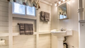 Un baño con un lavamanos blanco, dos toallas, una ventana decorada con un oso y un árbol, y un espejo.