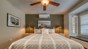 Un dormitorio con una cama grande, dos mesitas de noche, un ventilador de techo y una ventana con persianas.