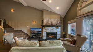 Una sala de estar con chimenea de piedra, un televisor grande y una escalera.