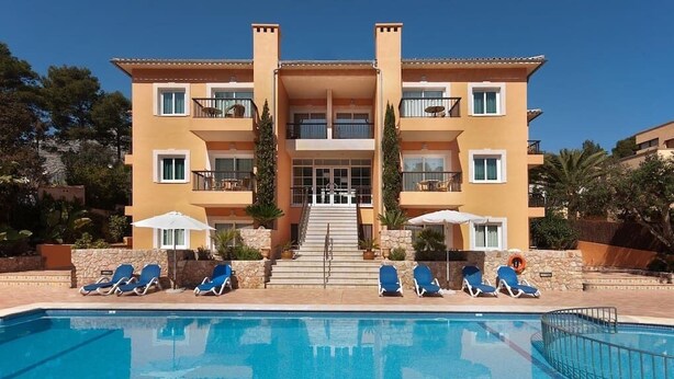Ein mehrstöckiges Hotel mit Schwimmbad, Außenbereich zum Sitzen und einer Treppe zum Eingang.