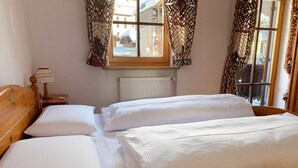Ein Zimmer mit zwei Einzelbetten, einem Holzkopfende, einem Nachttisch mit Lampe und einem Fenster mit gemusterten Vorhängen.