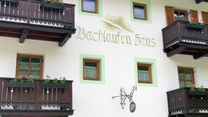 Ein Gebäude mit Balkonen, einem Schild mit der Aufschrift 'Bachlaufen Haus' und dekorativen Elementen.