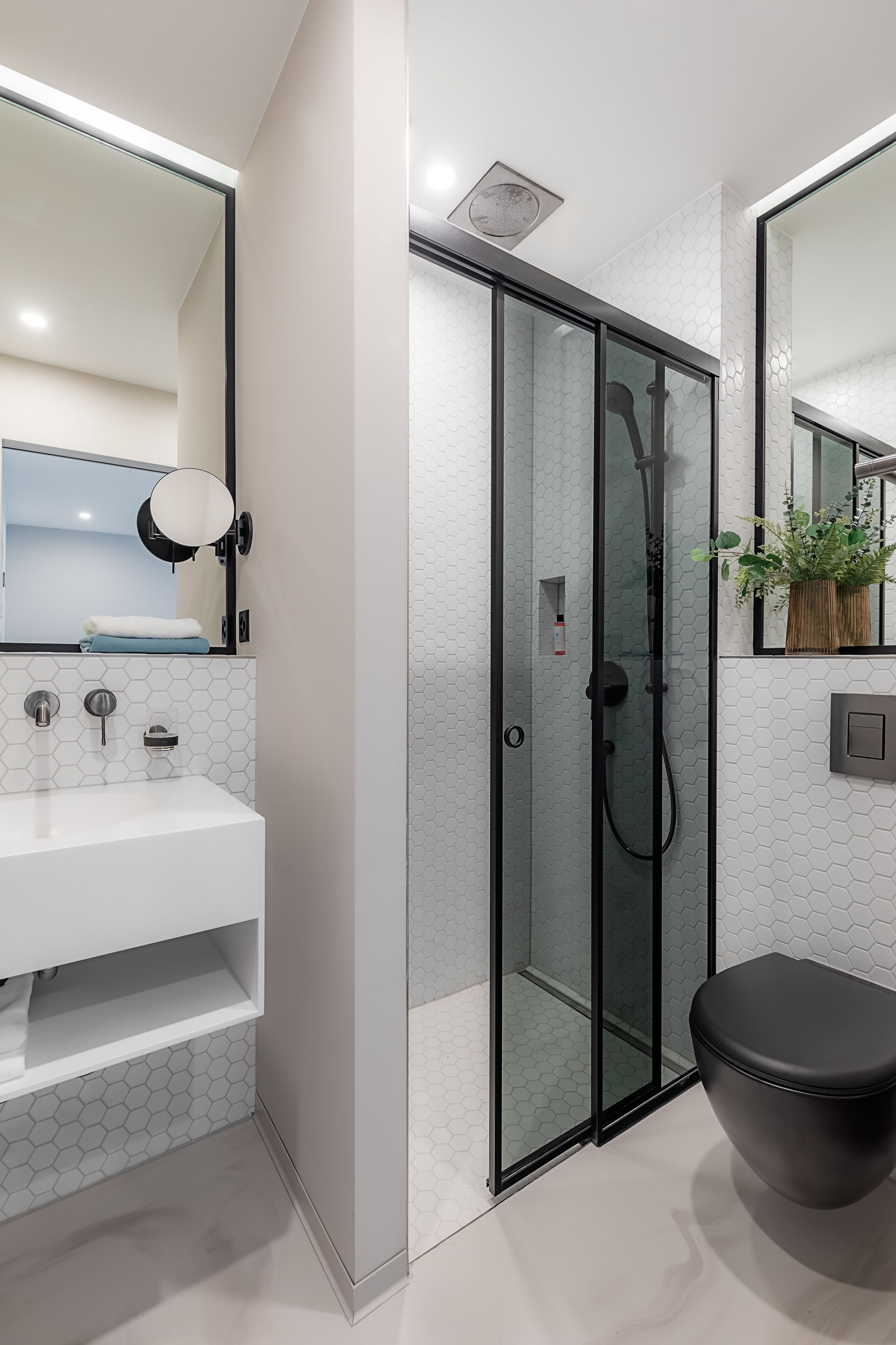 A modern bathroom with a glass-enclosed shower, a white sink, and a black toilet.