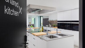 Una cocina moderna con armarios blancos, electrodomésticos de acero inoxidable y una isla central con pileta y tabla de cortar.