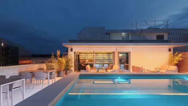 Un área de piscina en la azotea con mobiliario exterior y bar.