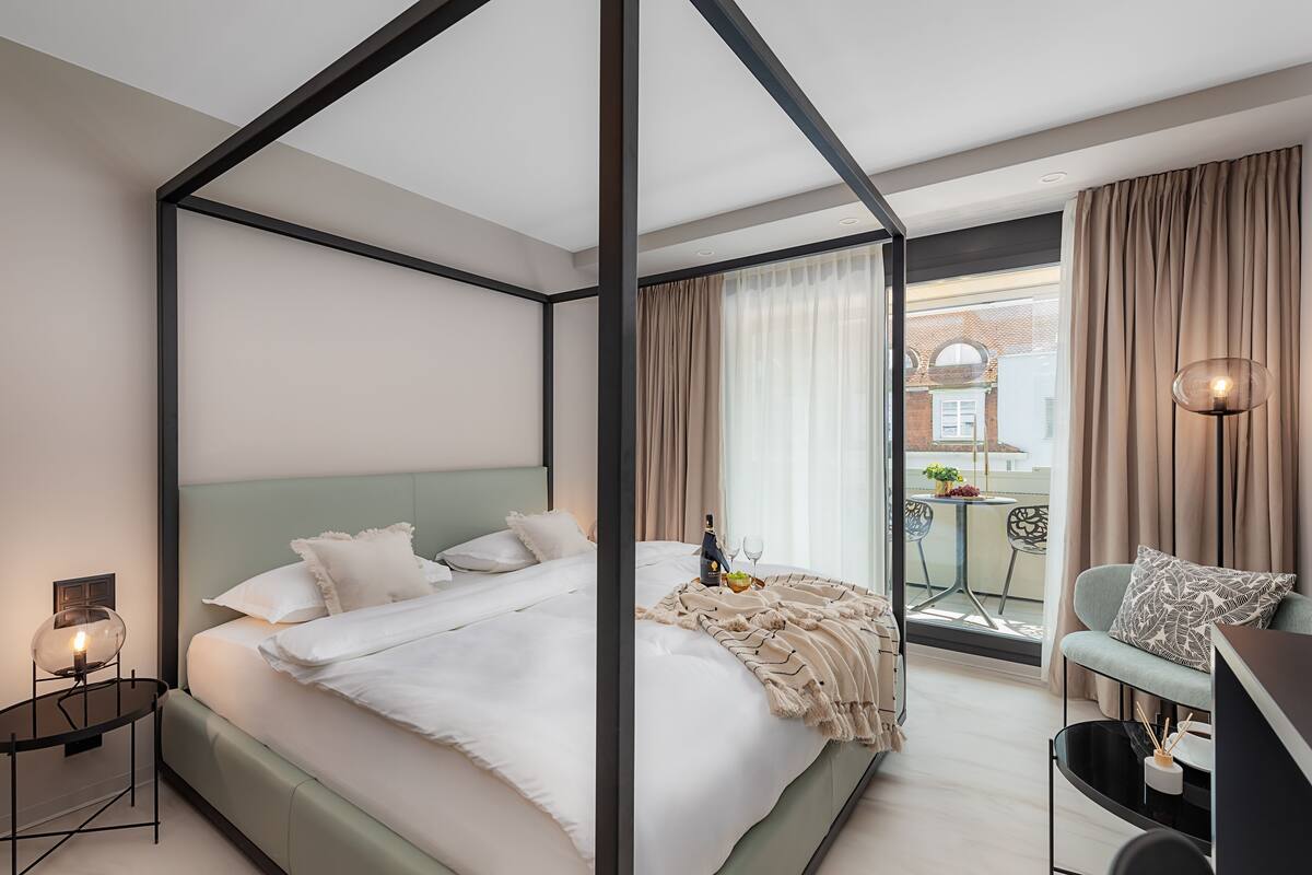 Et moderne hotelværelse med himmelseng, balkon med bord og stole samt byudsigt.
