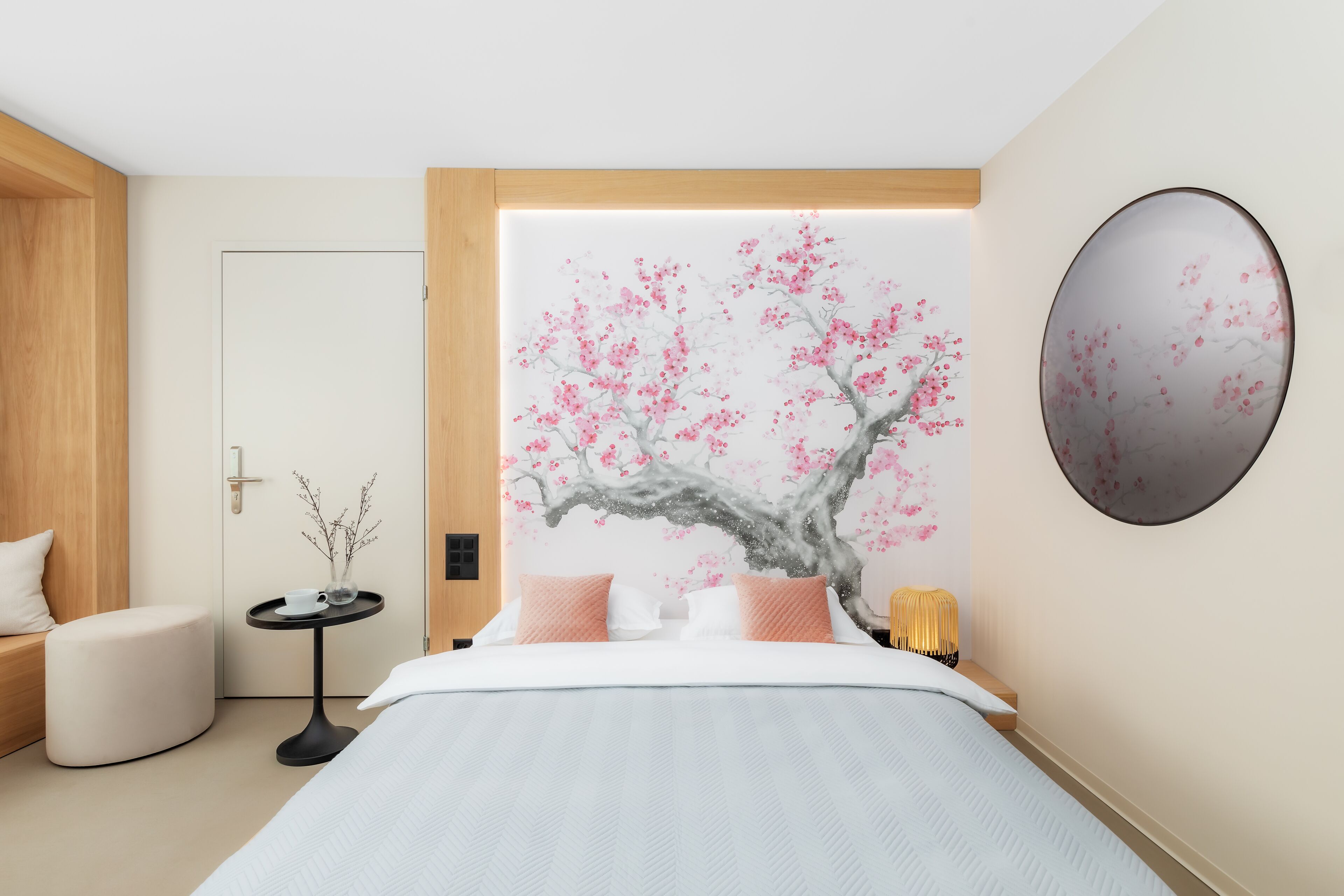 Un dormitorio moderno con una cama grande, una mesita redonda con un florero y un espejo montado en la pared.