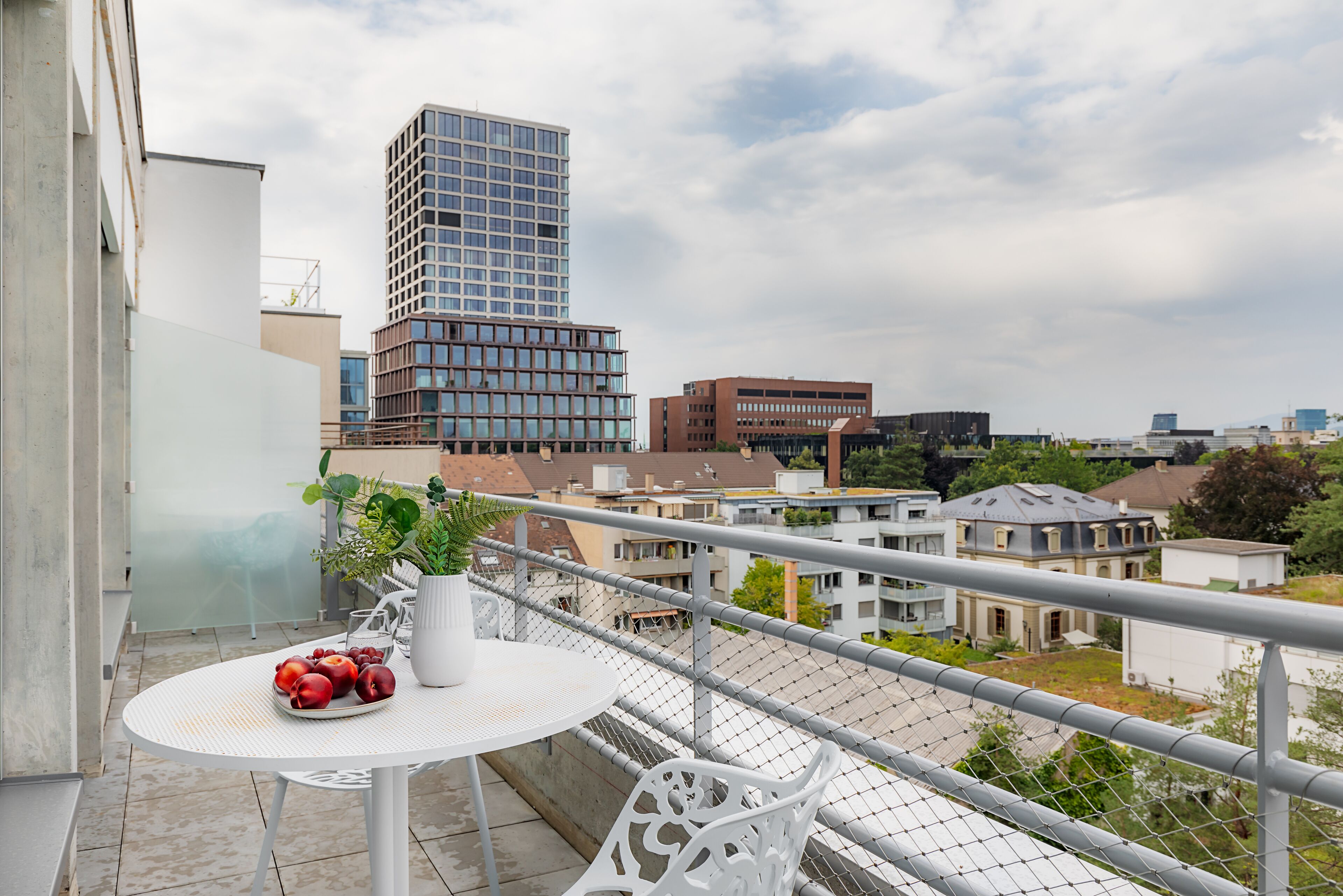 A balcony with a table, potted plant, and fruit bowl.
