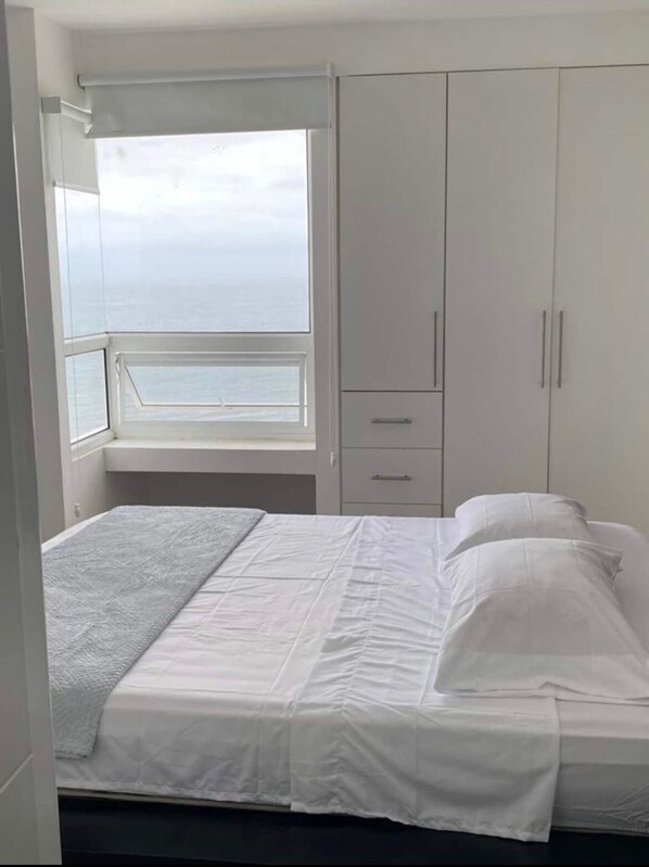 Un dormitorio con cama, ventana con vistas al mar y armario.