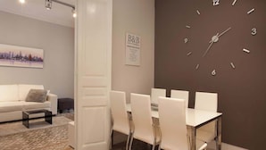 A modern living room with a white sofa, a coffee table, and a patterned rug. A dining area with a white table and chairs is visible, along with a wall clock. - Beautiful apartment to Enjoy the real Barcelona (Barcelona)