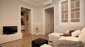 A living room with a TV, sofa, and coffee table. There is a kitchen in the background with cabinets and a microwave. - Beautiful apartment to Enjoy the real Barcelona (Barcelona)