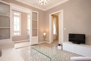 A modern living room with a glass coffee table, a flat-screen TV, and a patterned rug. - Charming apartment in a real Barcelona surrounding (Barcelona)
