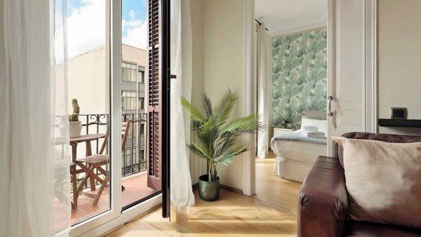 Un vaste espace de vie avec une porte-fenêtre coulissante donnant sur une terrasse extérieure, un canapé en cuir marron et une plante en pot.