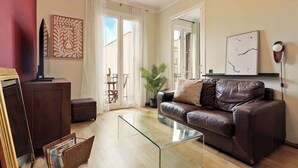 Un salon avec une table basse en verre, un canapé en cuir marron, un téléviseur et des œuvres d’art accrochées aux murs.