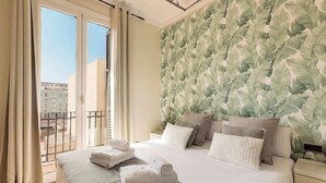 Une chambre d’hôtel avec un grand lit, un balcon avec des rideaux et un papier peint orné de motifs végétaux.