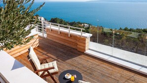 Una terraza de madera con barandilla blanca, una mesa con una bebida y una taza, y una silla.