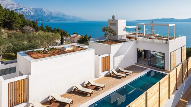 Un área de piscina moderna en la azotea con sillones de descanso y vistas al mar.