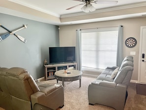 A living room with a television, a sofa, a coffee table, and a ceiling fan.