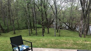 A patio with a black metal chair and a small table, surrounded by a grassy area and trees.