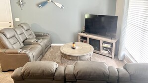 A living room with a leather sofa, a coffee table, a flat-screen TV on a wooden stand, and a wall-mounted compass decoration.