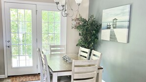 A dining area with a wooden table and chairs, a chandelier, a potted plant, and a painting on the wall.