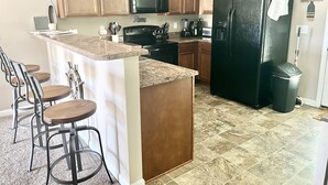 A kitchen with wooden cabinets, a black refrigerator, granite countertops, a microwave, a stove, and a coffee maker.